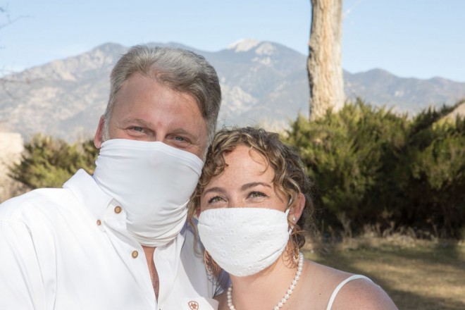 Rosie and Phil in front of Taos Mountain on their wedding day wearing white masks
