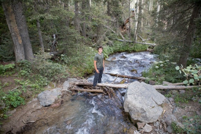 William smiles a photo while crossing the river on a hike in the Taos Ski Valley