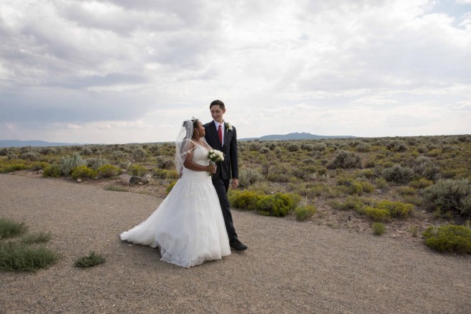 Bride and groom walk on mesa with Three Peaks in background in Taos, NM