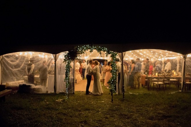 Bride and groom kiss in the subtly lit eucalyptus decorated doorway of their reception tent