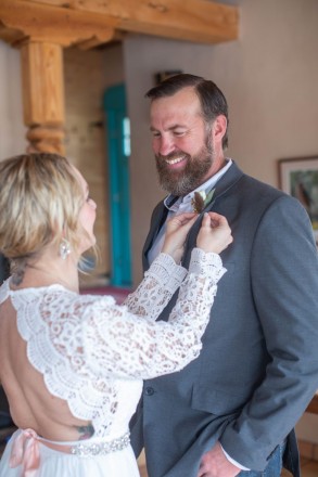 Linsey pins Nathan's boutonniere onto his collar before their private wedding elopement in the Questa mountains