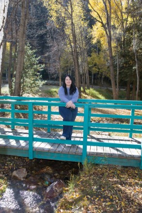 Katy stands on turquoise bridge with aspens and stream