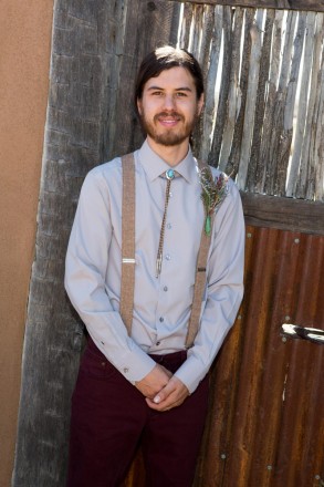 Groom with long hair, suspenders, a turquoise bolo tie, and a beard in front of NM door