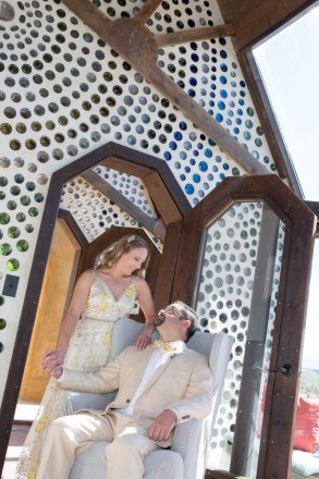 Wall made with bottles adorns the background of this Earthship wedding photo