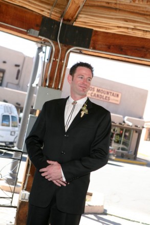 Groom, wearing a bolo tie, waits for his bride to walk to Taos plaza