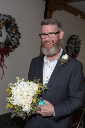 Groom, Justin, holds his wife's bouquet and smiles modeling her lipstick residue