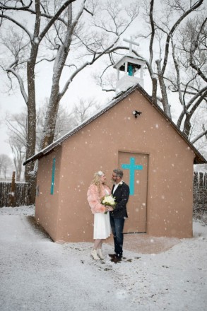 Newlyweds pose with bouquet under light snow under Taos Cottonwoods