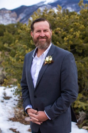 Nathan smiles in front of pinon tree in gorgeous cloudy light that on his wedding day