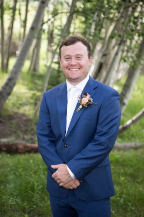 Groom, Clynt, wears a blue suit and a white tie for his July wedding