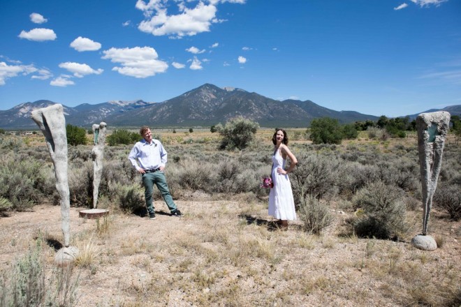 Blue skies and interesting art with bride and groom and beautiful Taos mountains