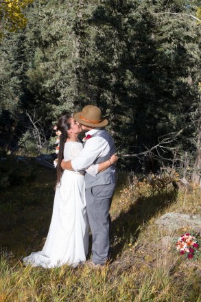 With the conifer trees looking on, the newlyweds share a kiss