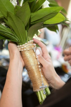 Maid of honor helps to put a rosary around bride's bouquet ribbon
