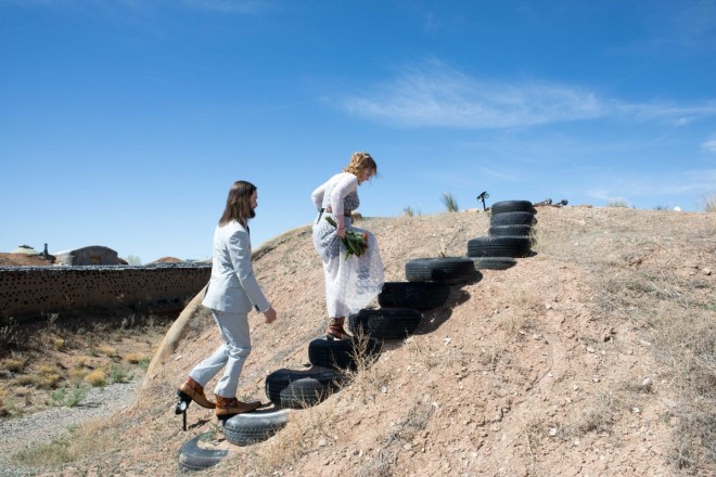 Bride and groom walk up recycled tire staircase at their Earthship wedding venue in Taos