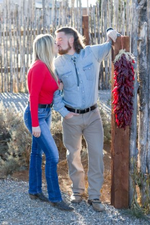 Engagement photos in cowboy boots next to chile ristra in Taos, NM