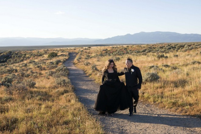 Bride and groom in black walk along the mesa at sunrise