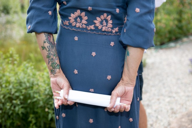 Susan, bride with tattoos, holds her wedding vows in a scroll behind her back.