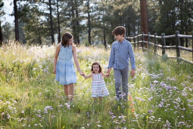 Older siblings help their younger sister walk through the wildflowers for a candid portrait