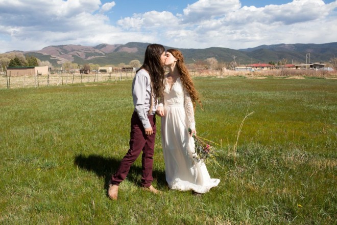 Hippie couple kiss on wedding day with Taos Pueblo hills in the background