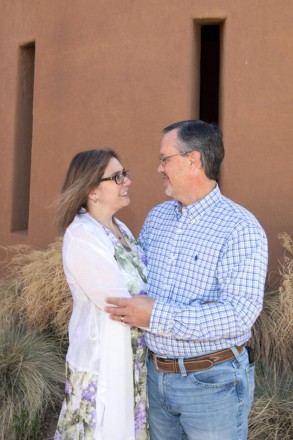 Couple poses in front of adobe home for photo shoot in Taos, NM