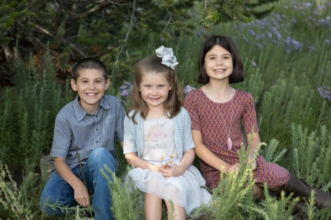 Three siblings posing in field of purple asters for family photos