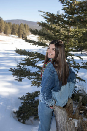 Senior in Class of 2022 leans against a stump with mountains of Angel Fire in background