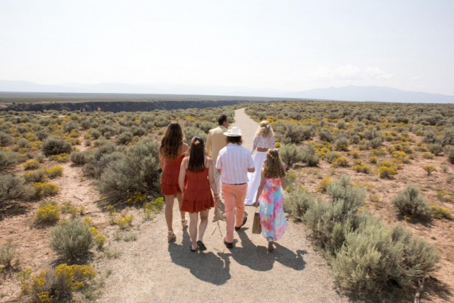 The family walks to their wedding site on path through sage and chamisa in Taos, NM