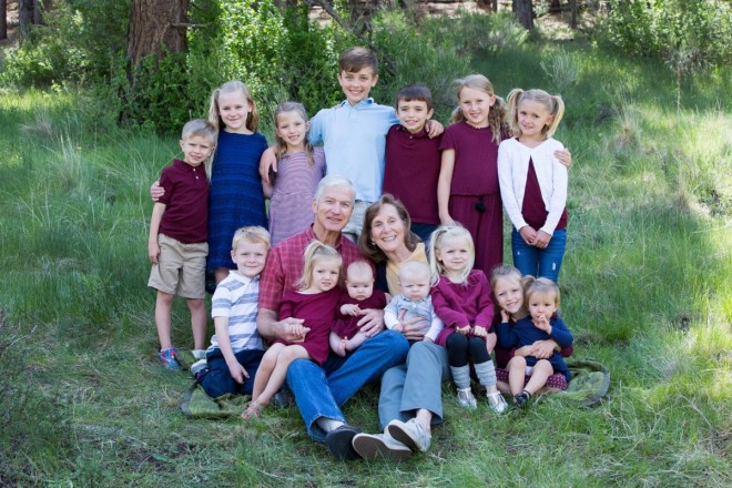 A proud grandma and grandpa smile with their 14 grandchildren during family portraits