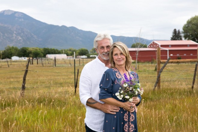 Susan and JR pose for a photo in front of red barn and Taos Mountain
