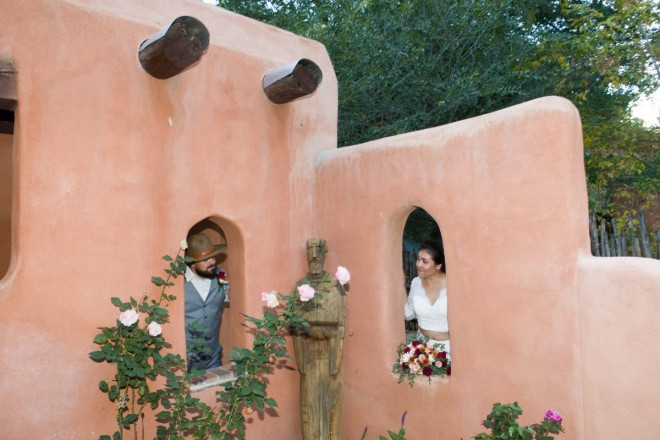 Newly weds look at eachother through pueblo-style architecture in Taos