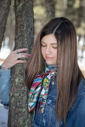 In a jean jacket and scarf, Angel Fire senior poses with mossy pine tree