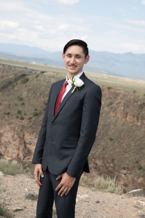 The groom with a red tie and a white rose in front of the Taos gorge