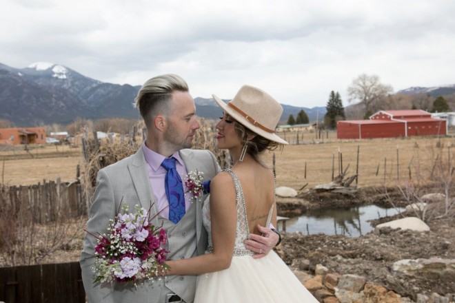Bride and groom with purple and lavender and red barn in front of sacred Taos Mountain