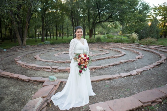 Bride with cascading bouquet standing with labyrinth in Taos