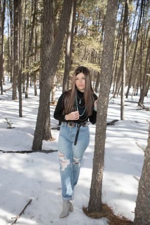 High school senior poses wearing ripped jeans, turquoise jewelry, and a black turtle neck