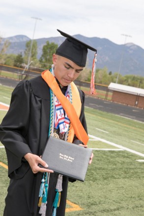 Taos graduate wearing his cap and holds his diploma on graduation afternoon
