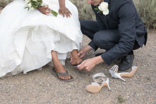 Groom helps his bride take off her high heels to put on her flip flops