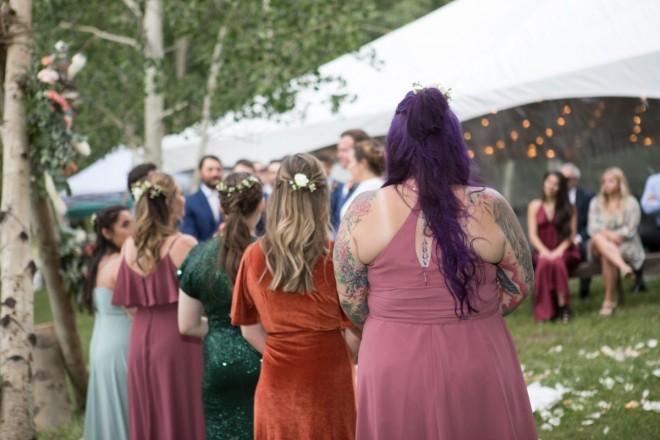 The backs of the bridesmaids during outdoor July wedding ceremony