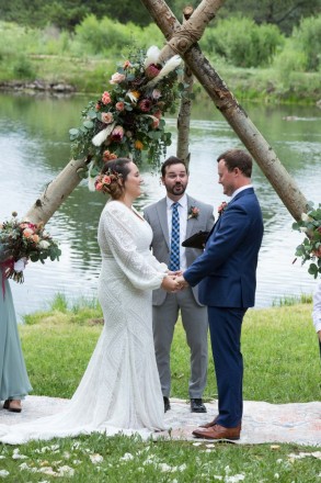 Wedding ceremony in front of pond with large altar flower arrangement in Taos, NM
