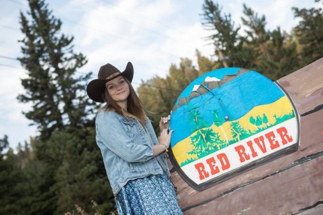 Katie poses with the Red River sign in her cowboy hat and jean jacket