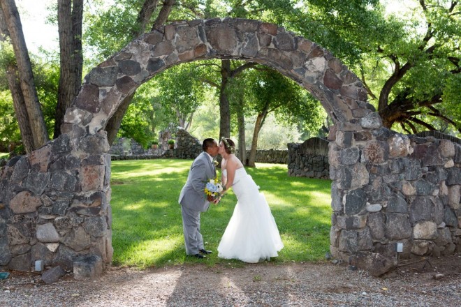 Bride and groom share a kiss under the archway at River Paradise Weddings in Embudo, NM