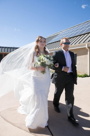 The wind plays with Victoria's veil as her dad walks her down the aisle