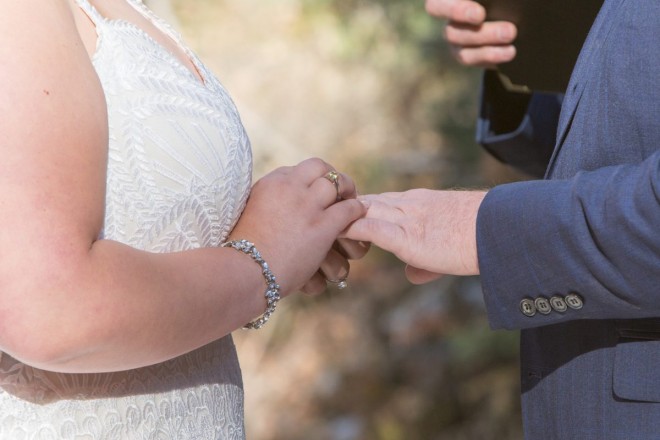 Sabrina places Joshua's ring on his finger at outdoor wedding ceremony