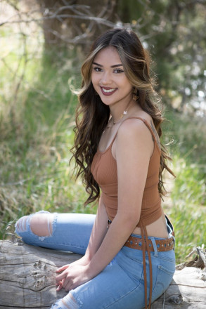 Long haired high school senior with tank top and ripped jeans sitting on dead cottonwood tree