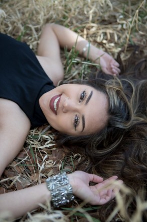 Senior, Jenica, smiles with her hair spread out on the forest floor.