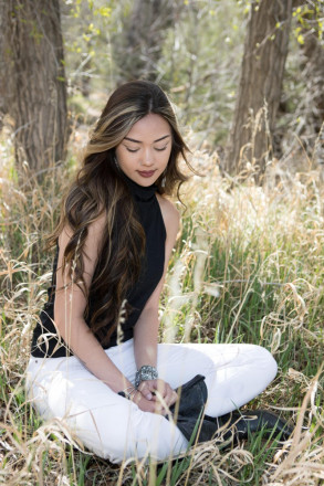 In white jeans and black boots, Jenica sits on the grass in the Carson National Forest