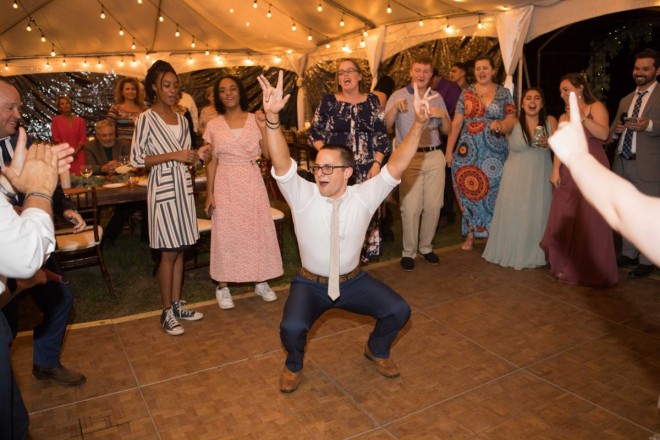 The brother of the bride has fun dancing in the middle of a circle at the reception
